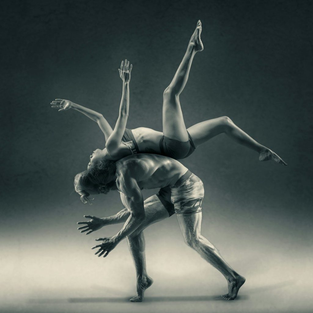 A woman flipping over a man, back to back